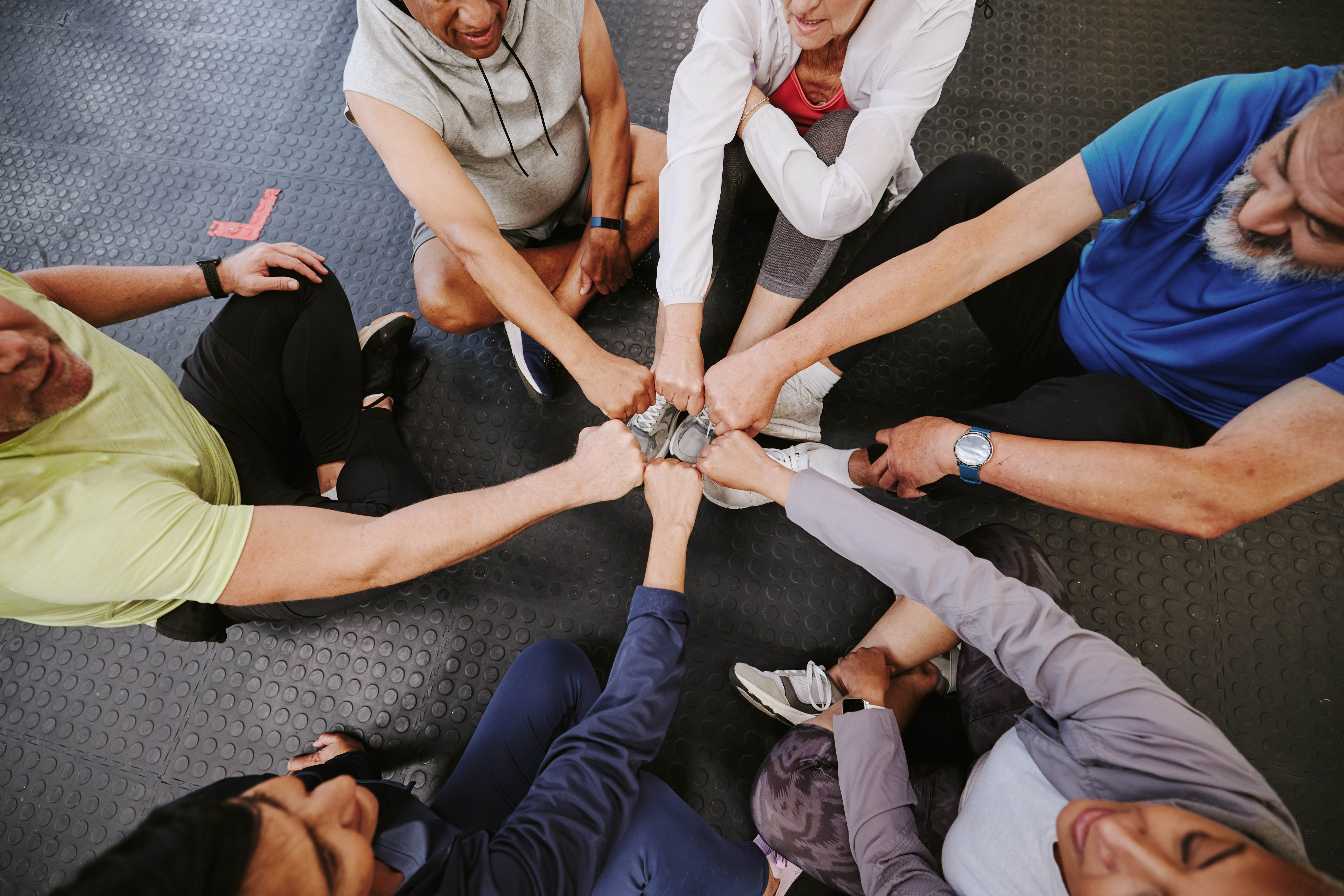 Group sitting on the gym floor with fists in the middle in greeting and celebration